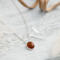  A playful 18" sterling silver necklace with a 10mm Baltic amber oval pendant on a light wood table, surrounded by soft decor. 
